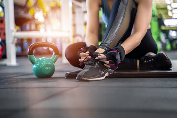 Young girl asian knelt down to do up her shoelaces at fitness gym after training sport with dumbbell