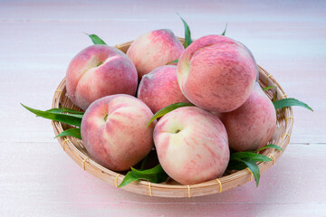 Fresh Sweet Peach on pink wooden  background, Pink and yellow Peach fruit with leaf on bamboo basket.