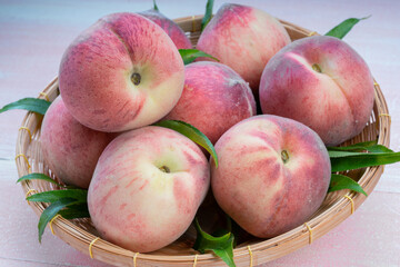 Fresh Sweet Peach on pink wooden  background, Pink and yellow Peach fruit with leaf on bamboo basket.
