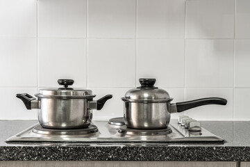 Couple of stainless pots on kitchen stove with marble counter top and white tile wall