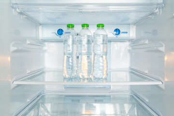 Cold bottles of clean drinking water in a white refrigerator