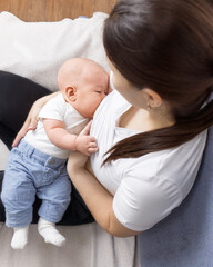 young asian woman breastfeeding baby sitting on sofa at home, breastfeeding, mother and baby at home, selective focus