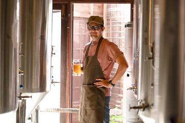 A young man works in a brewery and checks the quality of craft beer. The brewery owner tastes the best beers from Bach. A man's shortcut fills a glass of beer with