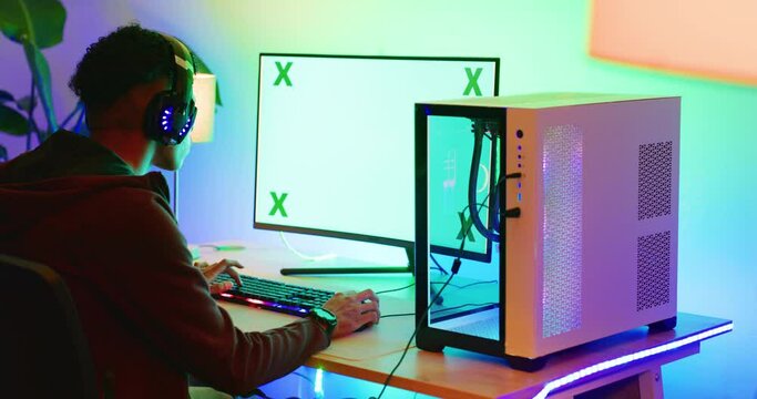 Green screen computer gamer wearing headphones and playing pc games in a home bedroom at night. Teenage boy sitting and using a copy space desktop monitor in a dark room for esports or virtual sports