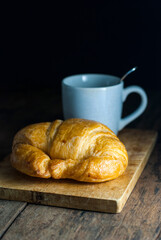 Butter croissant with a cup of coffee put on a wooden cutting board on a rustic wooden floor.