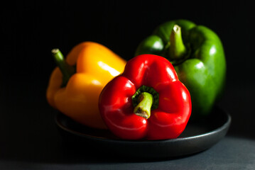 Colorful of bell peppers, green, red, yellow in a black ceramic tray on a black background.