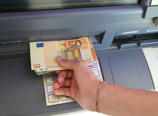 hand taking euro banknotes from an ATM after typing the code