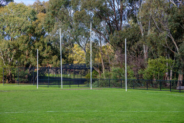 Australian Football League goal posts in a suburban sports oval with cricket practice nets in the background