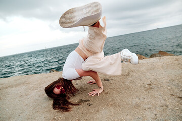 Female dancer doing handstand while breakdancing outdoors against sea.