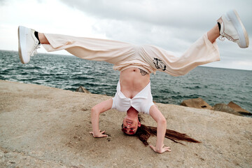 Young dancer doing handstand while dancing freestyle against the sea.