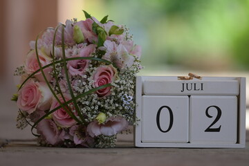 Brautstrauß liegt neben Hochzeits-Datum aus Holz 02. Juli mit Eheringen