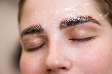 Caucasian woman on the procedure of permanent styling and coloring of eyebrows.