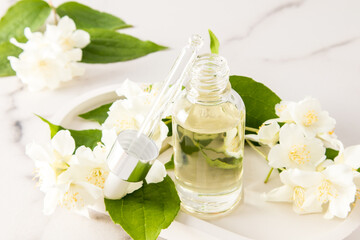 an open bottle with a dropper of cosmetic organic jasmine oil on a background of flowers for face and body skin care. relaxation. phytotherapy.