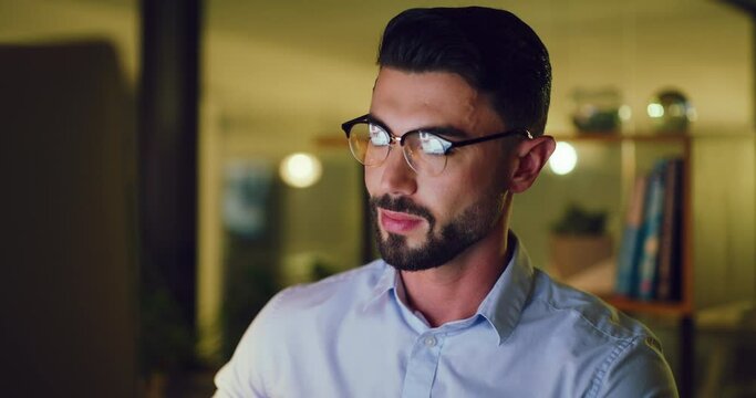Young business man working late on a computer in an office at night. Face of a hardworking entrepreneur reading emails, doing research online and compiling reports while planning ideas for deadlines