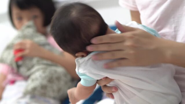 Mother burp newborn baby boy. Background is sister.