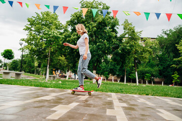 A young beautiful teenage girl rides a skateboard on a beautiful summer day in the park. A girl enjoys skateboarding outdoors. An active lifestyle.