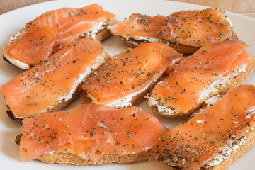 Detail of a slice of toasted bread with cheese spread and smoked salmon with basil on a canapes tray.