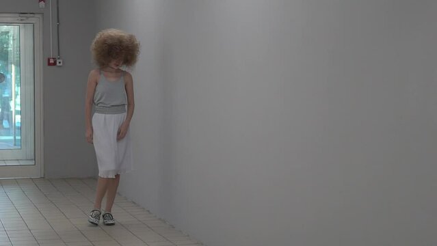 Slow Motion young activity woman with blond curly afro hair against the wall