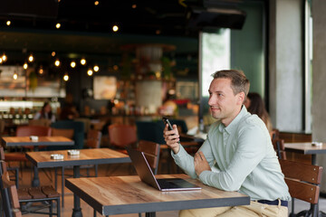 Confident businessman using smartphone sitting in restaurant