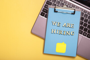 Wooden letters with phrase we are hiring on clip-board on colored background top view. Search worker concept