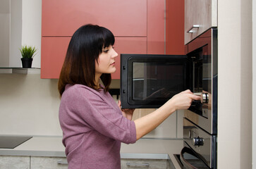 A young woman takes a plate out of the microwave.