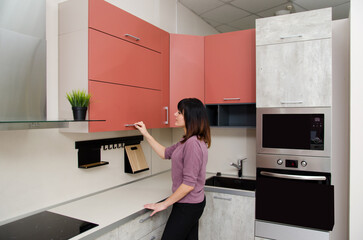 A young woman opens the kitchen cabinet door by the handle.