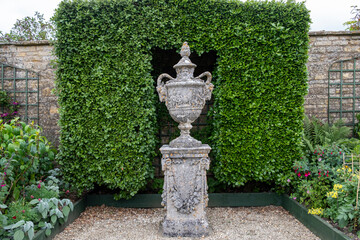 Stone urn and topiary hedge at Bourton House gardens, Morton in Marsh. market town in the...
