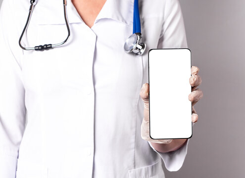 Doctor holding phone with screen mockup. Online medicine, using medical application in smartphone, telehealth, telemedicine concept. Woman in lab coat with stethoscope and gloves. High quality photo