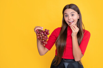 glad amazed teen child hold bunch of grapes on yellow background