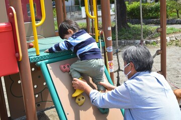 公園の小さなボルダリングを登る幼児と祖父　2歳