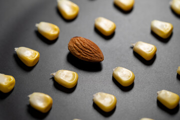 Corn kernel place neatly in rows and a piece of almond on a black round plate.
