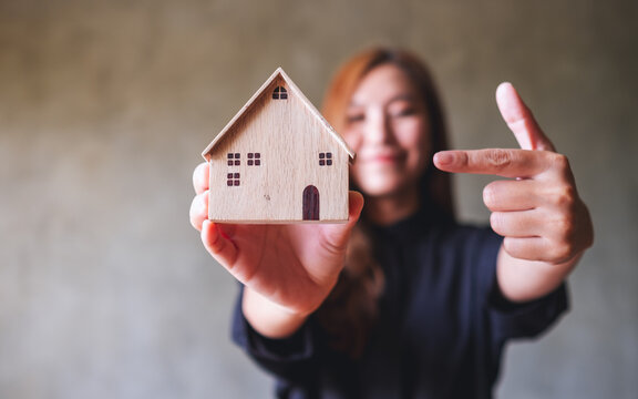 A young woman holding, showing and pointing finger at a wooden house model