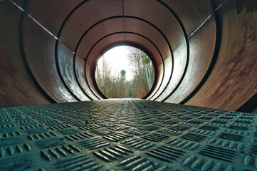 View through a metal pipe. In the background between trees is a water tower.