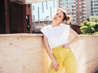 Young beautiful smiling hipster woman in trendy summer yellow jeans clothes. Carefree teen model posing in the street at sunset. Positive female outdoors. Cheerful and happy. In sunglasses