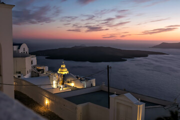 Fototapeta premium Panoramic view of the volcano, the illuminated village of Fira and a stunning sunset of the Aegean Sea in Santorini