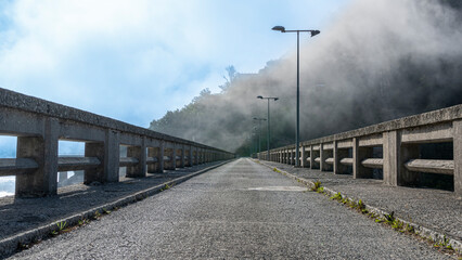 Fototapeta premium Carretera sobre presa de un pantano y bruma a primera hora de la mañana en la montaña Palentina, España