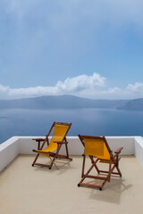 Fototapeta na wymiar View of two empty sunbeds on the rooftop of a villa and a spectacular view of the Aegean Sea in Santorini Greece
