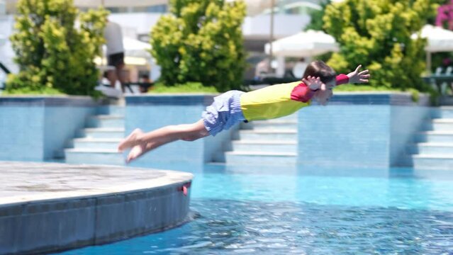 Child falling into a summer outdoor pool. kid relaxing during summer vacation. Boy jumping in pool and splashing crystal clear water in basin at sunny day.