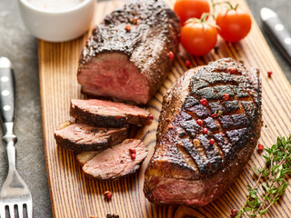 Juicy delicious fragrant Roast duck breast medium rare on a wooden board with pepper and cherry tomatoes.