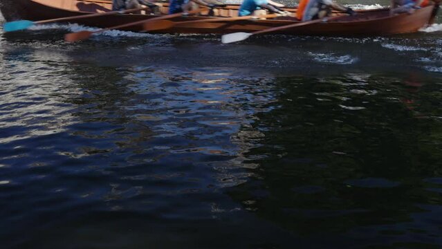 A wooden boat with rowers floats on the Klaipeda canal. Rhythmic strokes with oars create splashes on the water. Beautiful movement of waves with reflections. Lithuania