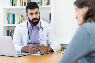 Concerned mature doctor with hipster beard talking with patient