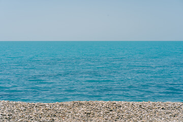 Bank of pebbles with the sea and beach in the background.