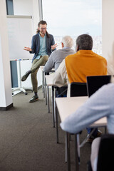 A young professor teaching a group of multicultural senior students using modern technologies.