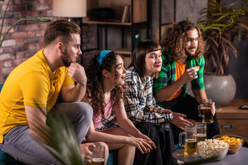Caucasian friends watching together a football match they cheering and cheers with beers for favourite team they sitting in front of tv