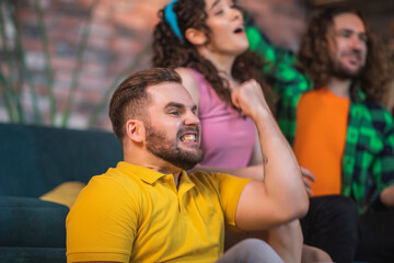 Fototapeta premium In living room in front of tv happy good looking group of young students multiracial getting together to watch a sport match on tv channel all together they enjoy the time together