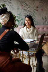 Two happy multicultural female college girls are sitting in cafeteria and studying for an exam.