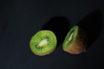 whole kiwi cut in half on a black background
