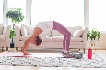 Woman in sports pink leggings and white top training at home and doing arch exercise alone at home