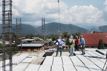 Construction site crane is lifting a precast concrete wall panel to installation building.