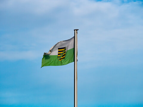 Saxony flag with coat of arms fluttering in the wind. Blue sky in the background. White green colors on the textile. German culture of the federal state system. National politics of the government.